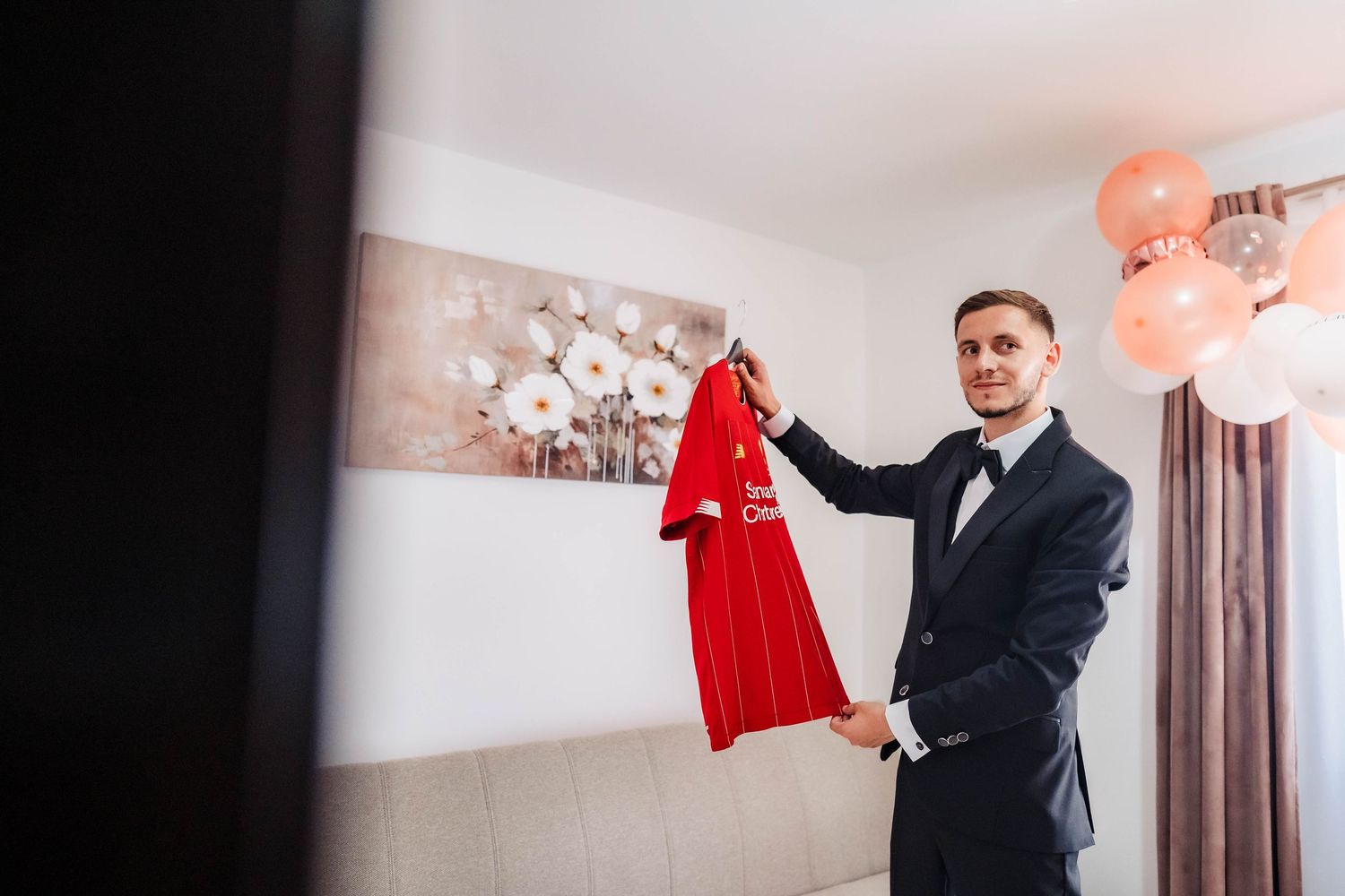 Wedding party members in formal attire holding up red dresses in a light-filled room.