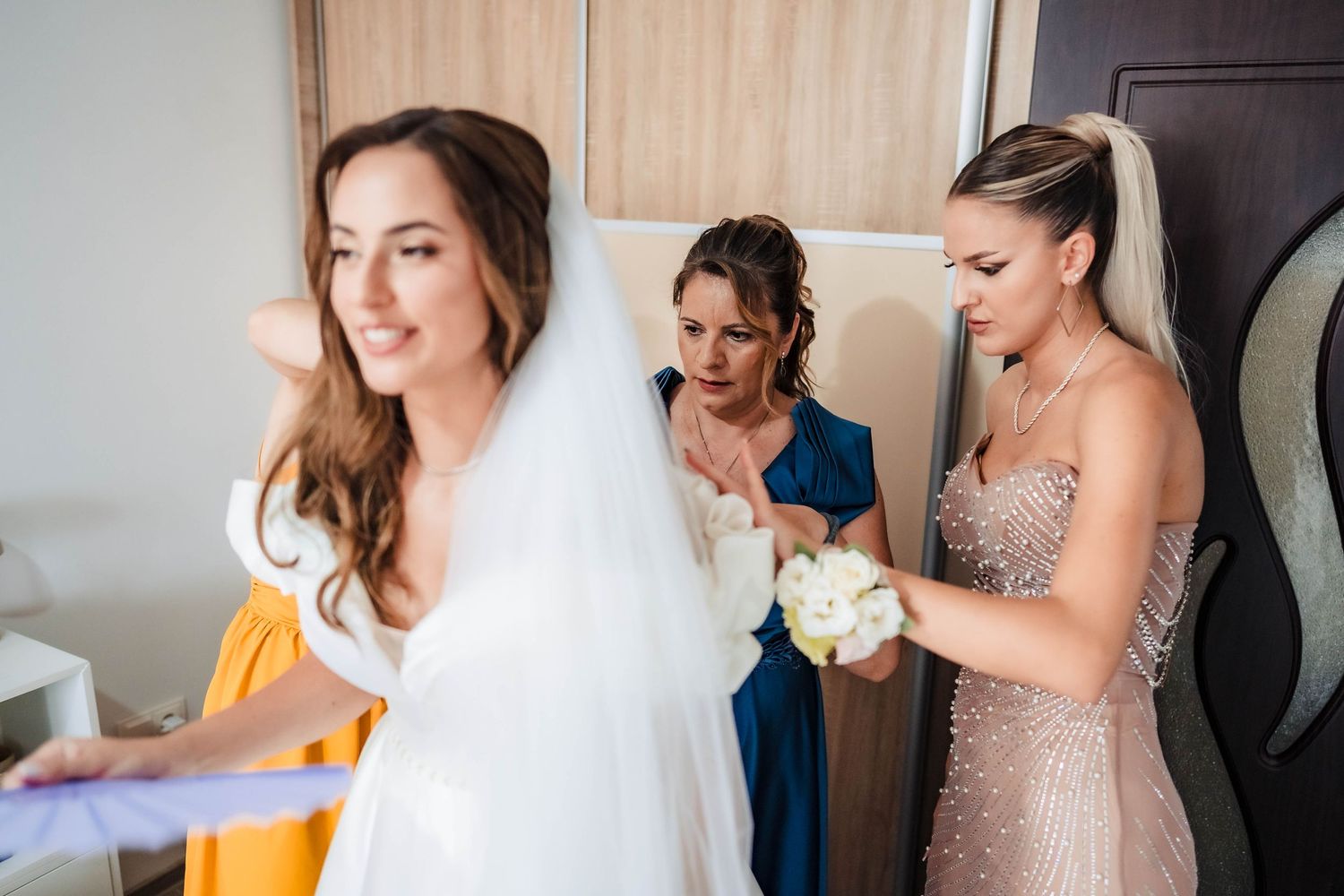 Wedding preparation scene showing bridesmaids helping with final touches in a bright room.