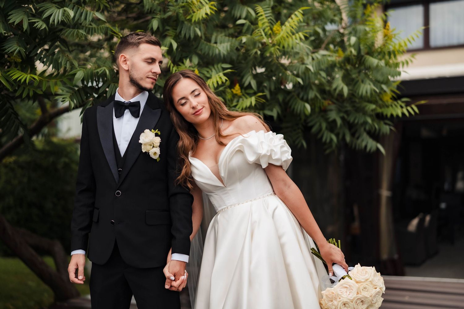 Elegant bride and groom share romantic moments in an outdoor garden setting with lush greenery.