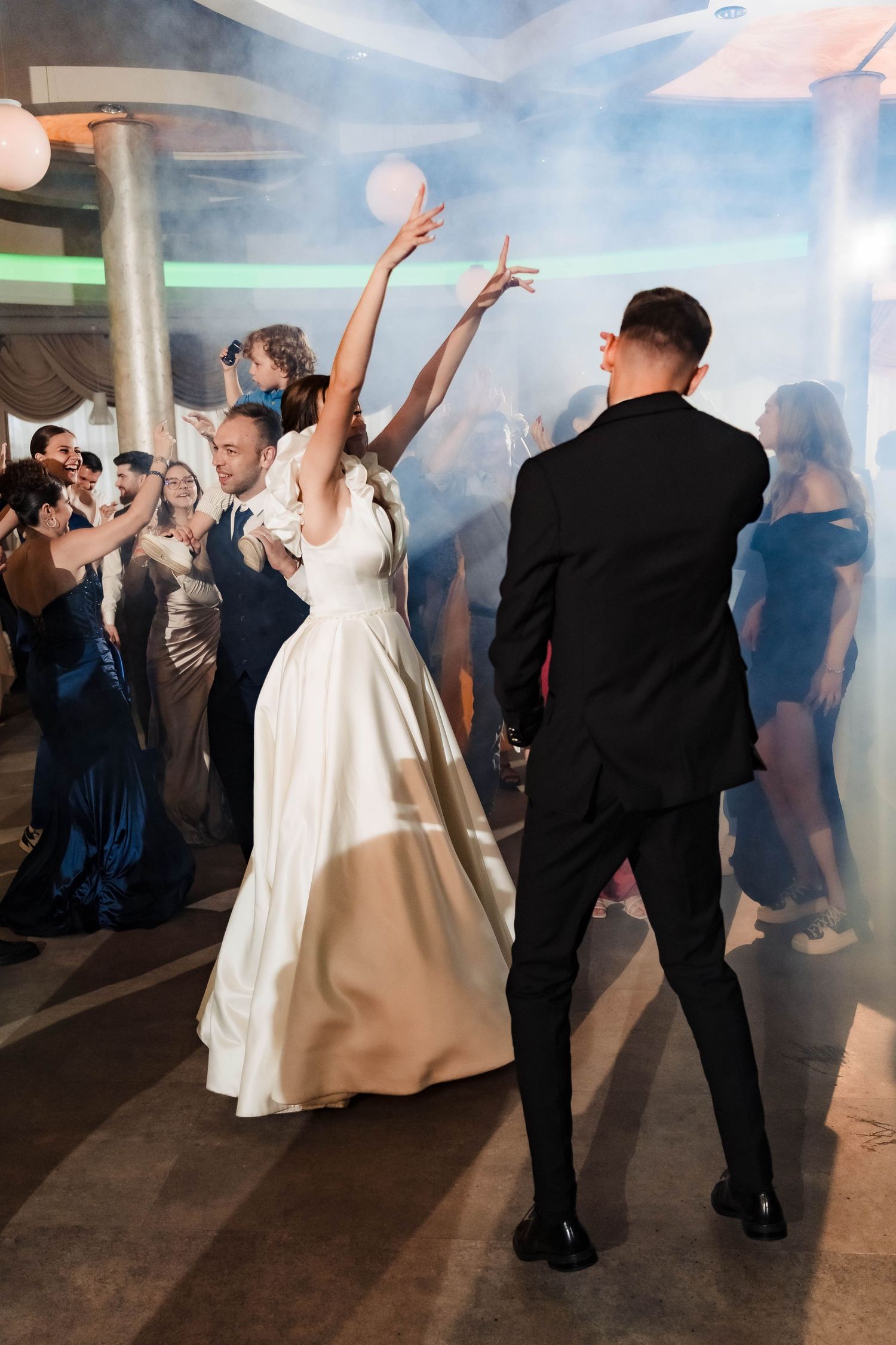 Wedding couple dances energetically in a misty reception venue with dramatic lighting effects.