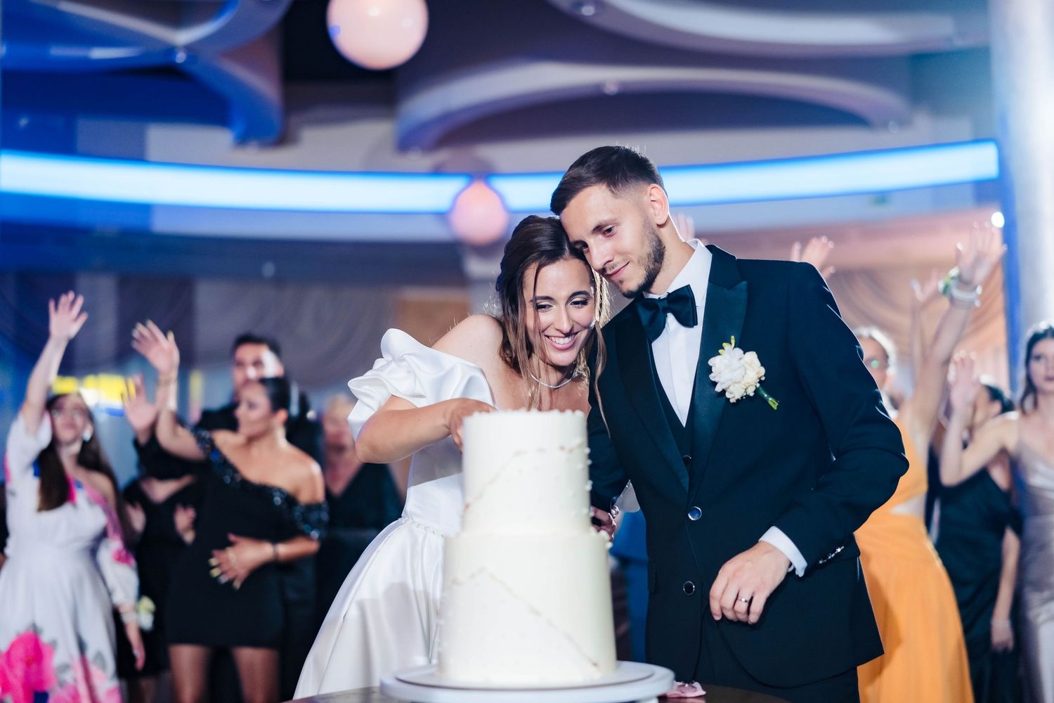 Wedding reception dance floor filled with celebrating guests under blue lighting.