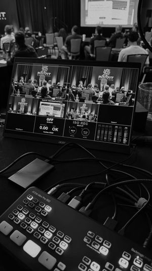 Video production control room setup showing multiple camera feeds on a monitor and a switcher board in the foreground.