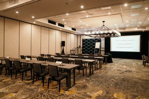 A panoramic view of a modern conference room with dark tables, chairs and projector screens arranged in rows.