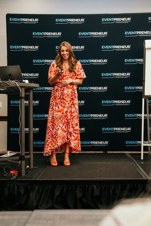 Speaker presents on stage at Eventpreneur conference with blue branded backdrop and podium.