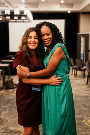 Two friends share warm hugs and laughter in a series of candid moments wearing burgundy and teal dresses.
