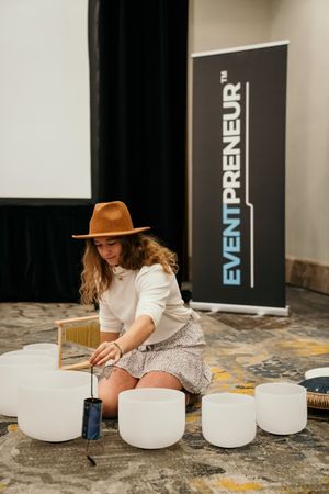 Person in white dress arranges multiple crystal singing bowls on a gray textured surface.