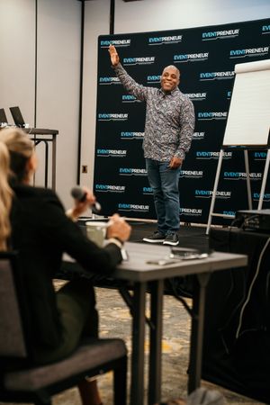 Conference speaker engages with audience at Eventpreneur event in front of branded backdrop display.