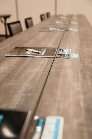 Notebooks and papers arranged on a wooden conference table with shallow depth of field.