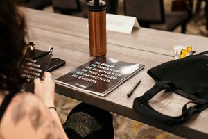 A hand writes in a journal with a fountain pen on a dark wooden desk illuminated by warm lighting.