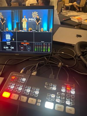 Professional video production setup showing an ATEM Mini control panel and MacBook with live streaming interface on display.