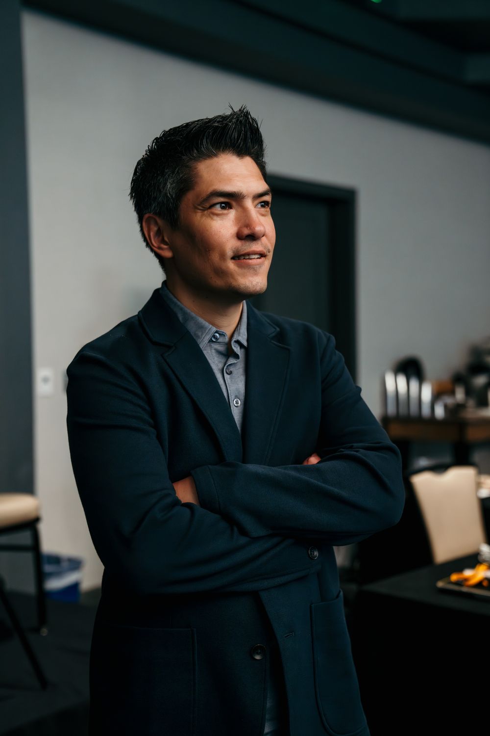 Professional in a navy suit gazes thoughtfully into the distance while seated in a modern office setting.