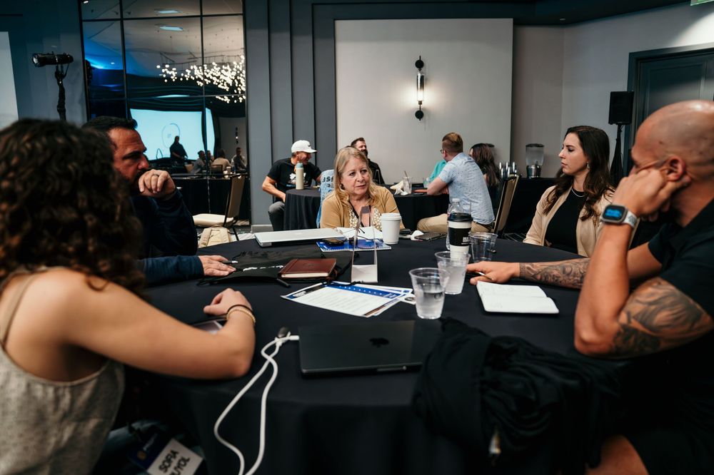 Business professionals seated at tables during a conference or meeting in a modern office space.
