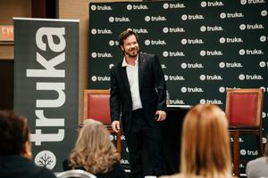 A speaker in a dark blazer presents on stage at an event with Trulia branding visible in the background.