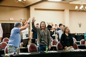 Enthusiastic attendees celebrate with high fives during a conference session in a hotel meeting room.
