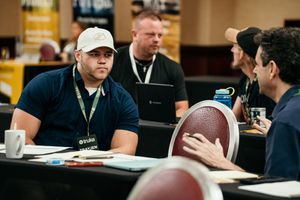A group of people sitting at tables during a business meeting with papers and a football visible on the desk.