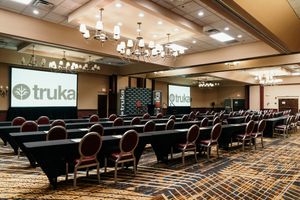 Modern conference room with rows of black chairs and patterned carpet features warm lighting and wood-paneled walls.