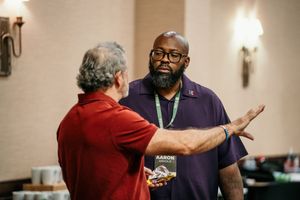 Two men engaged in animated conversation at an indoor professional event.
