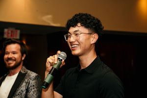 People laughing and smiling while performing at a dimly lit indoor venue with stage lighting.