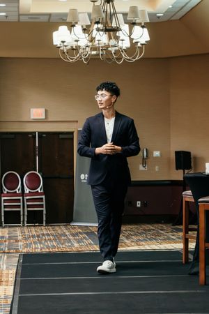 A series of photos showing someone in a dark suit dancing and moving across a carpeted banquet room with chandeliers.