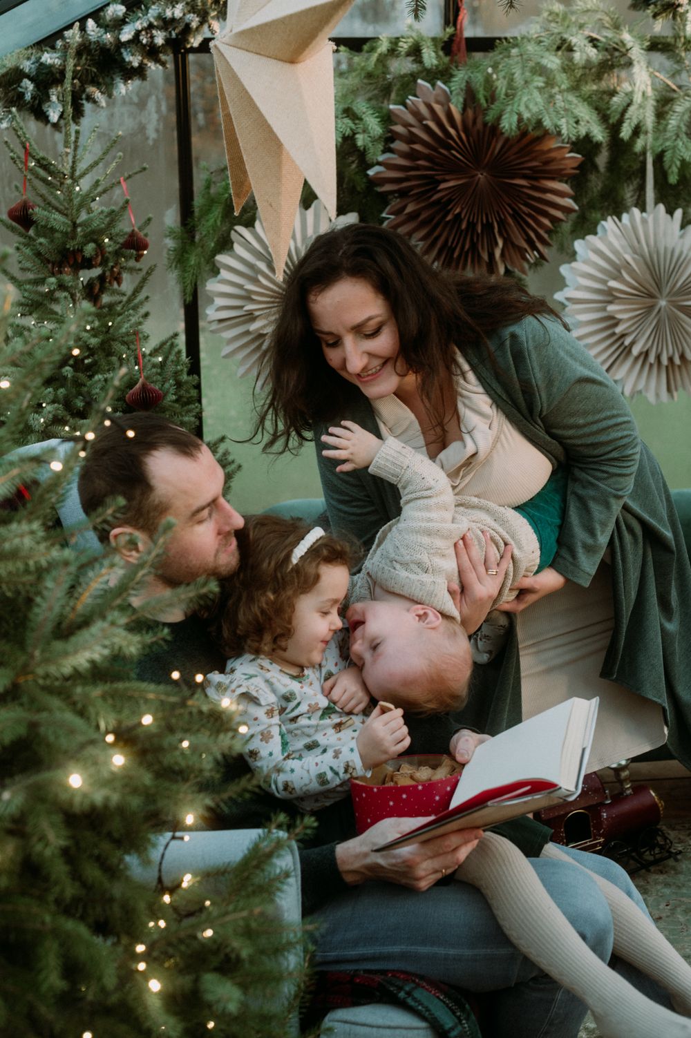 A festive family cuddle session on the floor with holiday decorations and Christmas trees in the background.