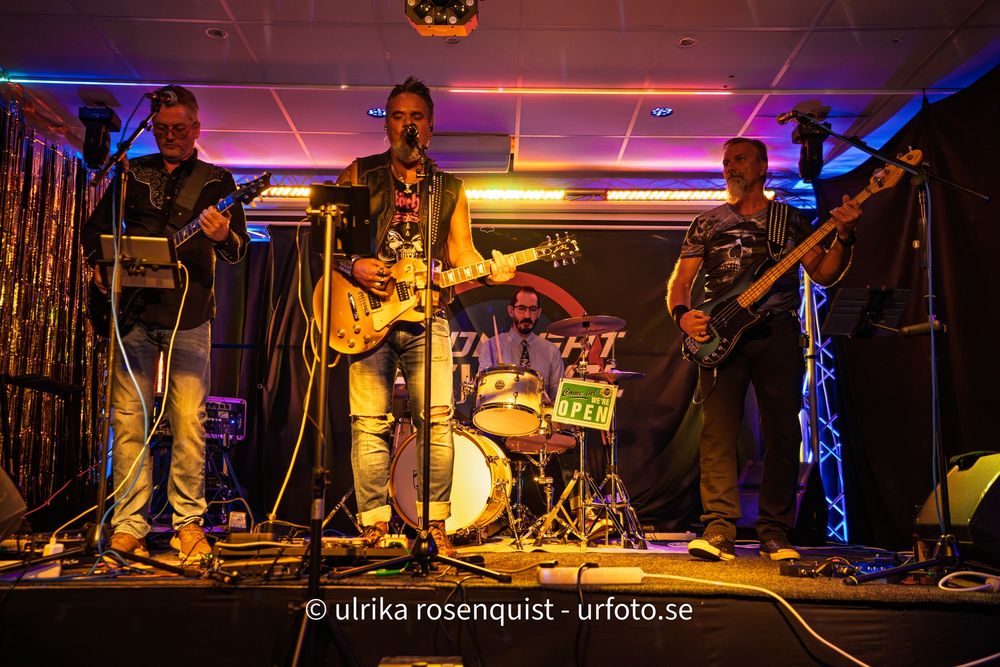 Musicians perform on stage with colorful blue and purple lighting at a live concert venue.