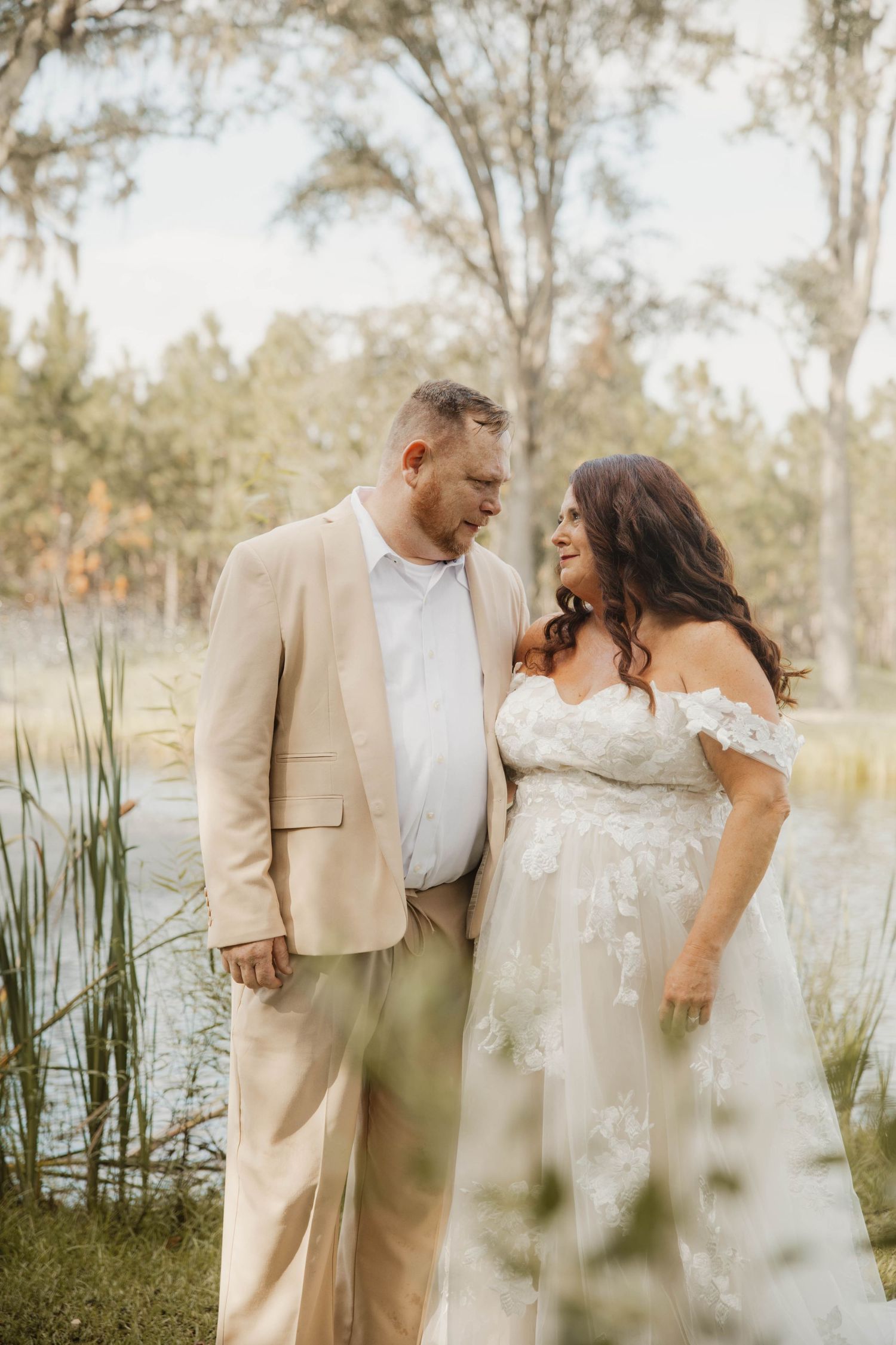 A romantic wedding photo collection showing a couple in natural lighting by a lake wearing beige and white attire.