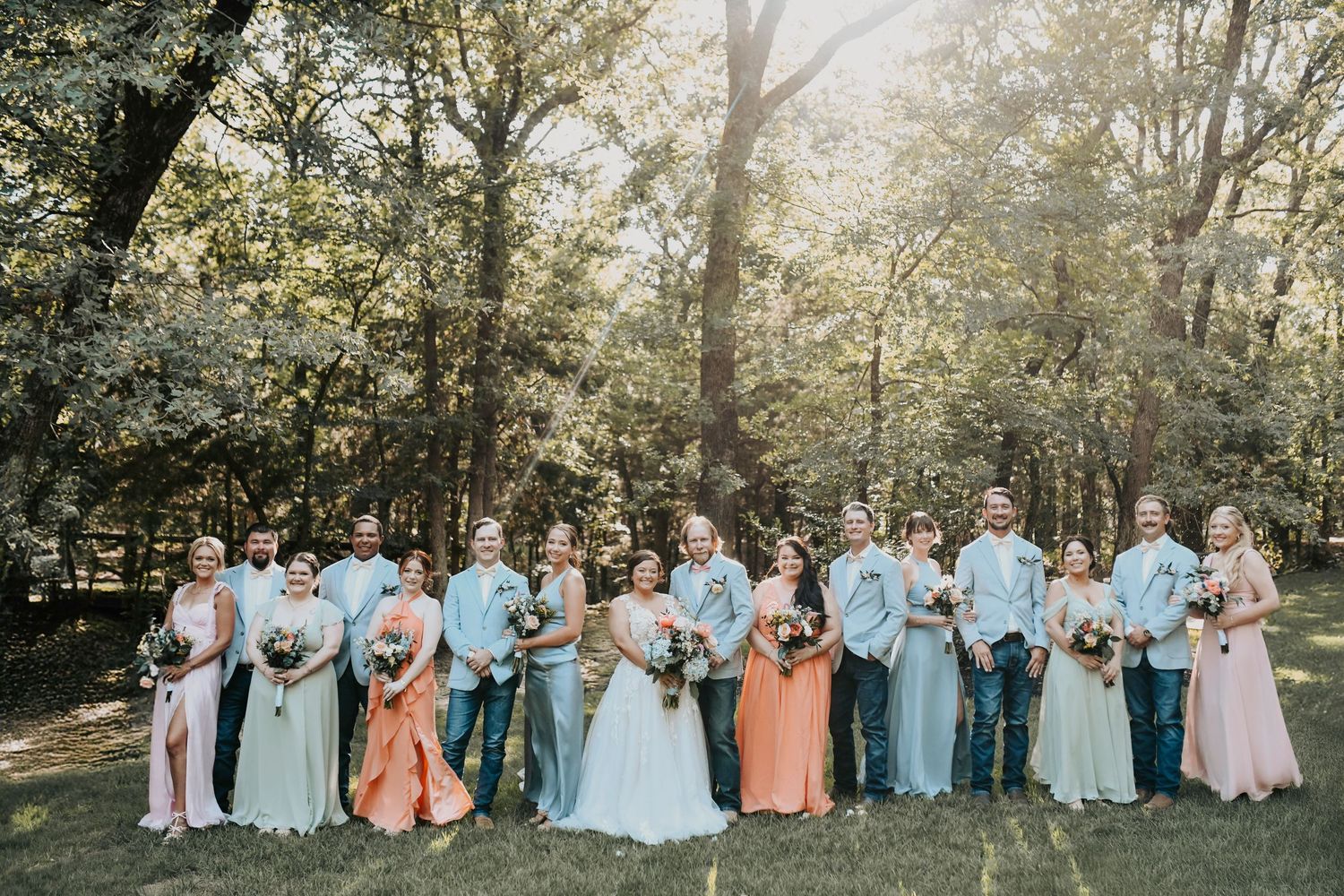 Full wedding party posing on Whispering Oaks wooden bridge