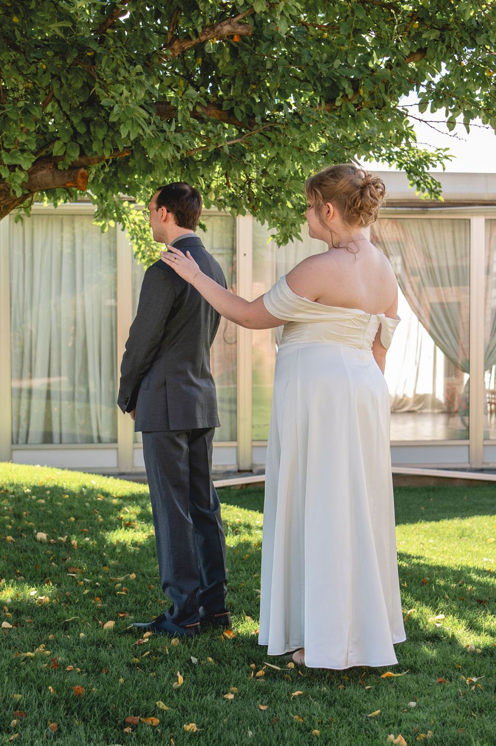 Couple in wedding attire sharing a tender moment under a leafy tree on a sunny day.