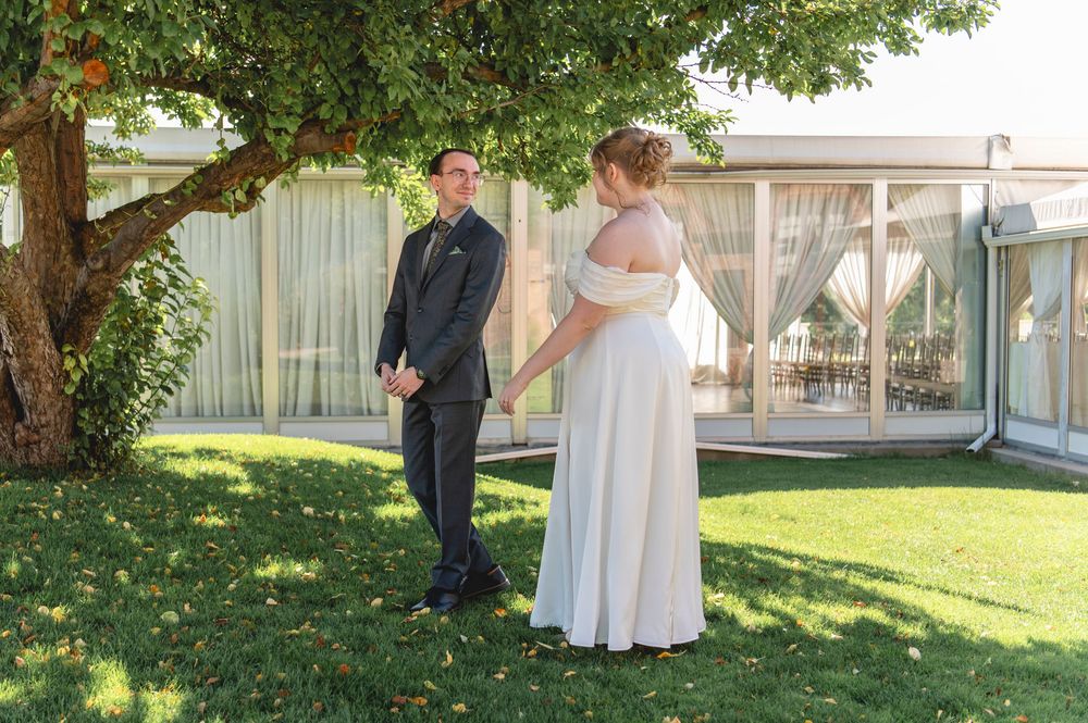 Two people stand in a garden setting during a wedding ceremony with a white tent and green grass visible.