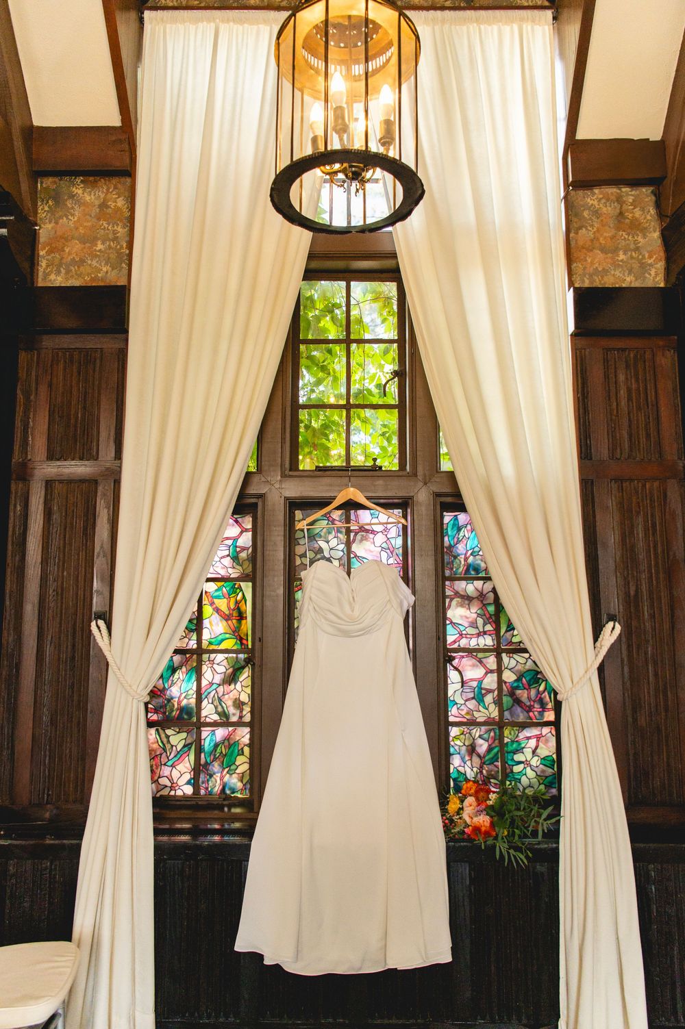 Beautiful stained glass windows and white curtains decorate wood-paneled walls in a vintage-style interior.