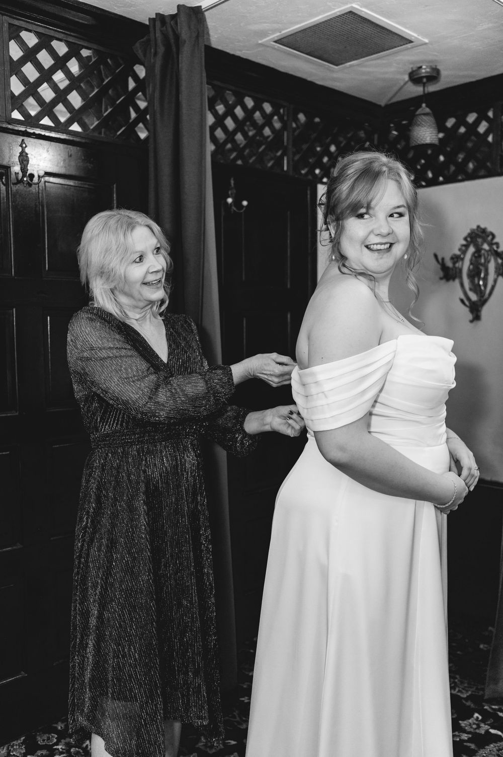 A touching black and white moment as someone helps adjust a wedding dress on a bride during preparations.