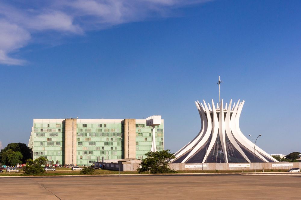 Brazilian architectural landmark Cathedral of Brasilia and surrounding government buildings against a blue sky with clouds.
