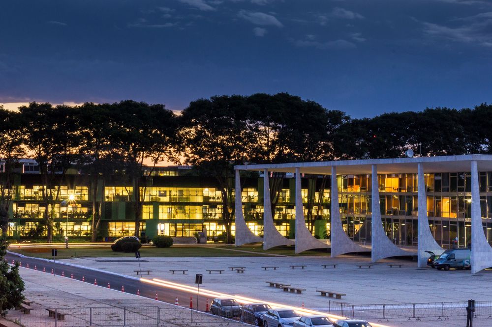 Long exposure panoramic nighttime view of an illuminated lakeside resort with buildings reflected in calm waters.