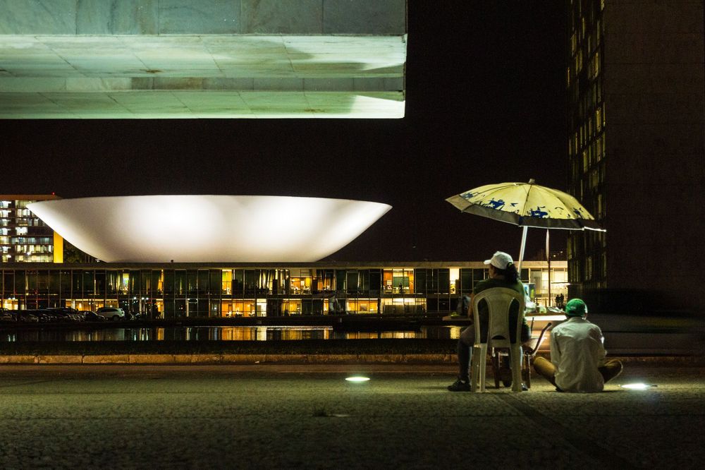 Night view of modernist architecture with illuminated glass walls and geometric forms creating dramatic shadows.