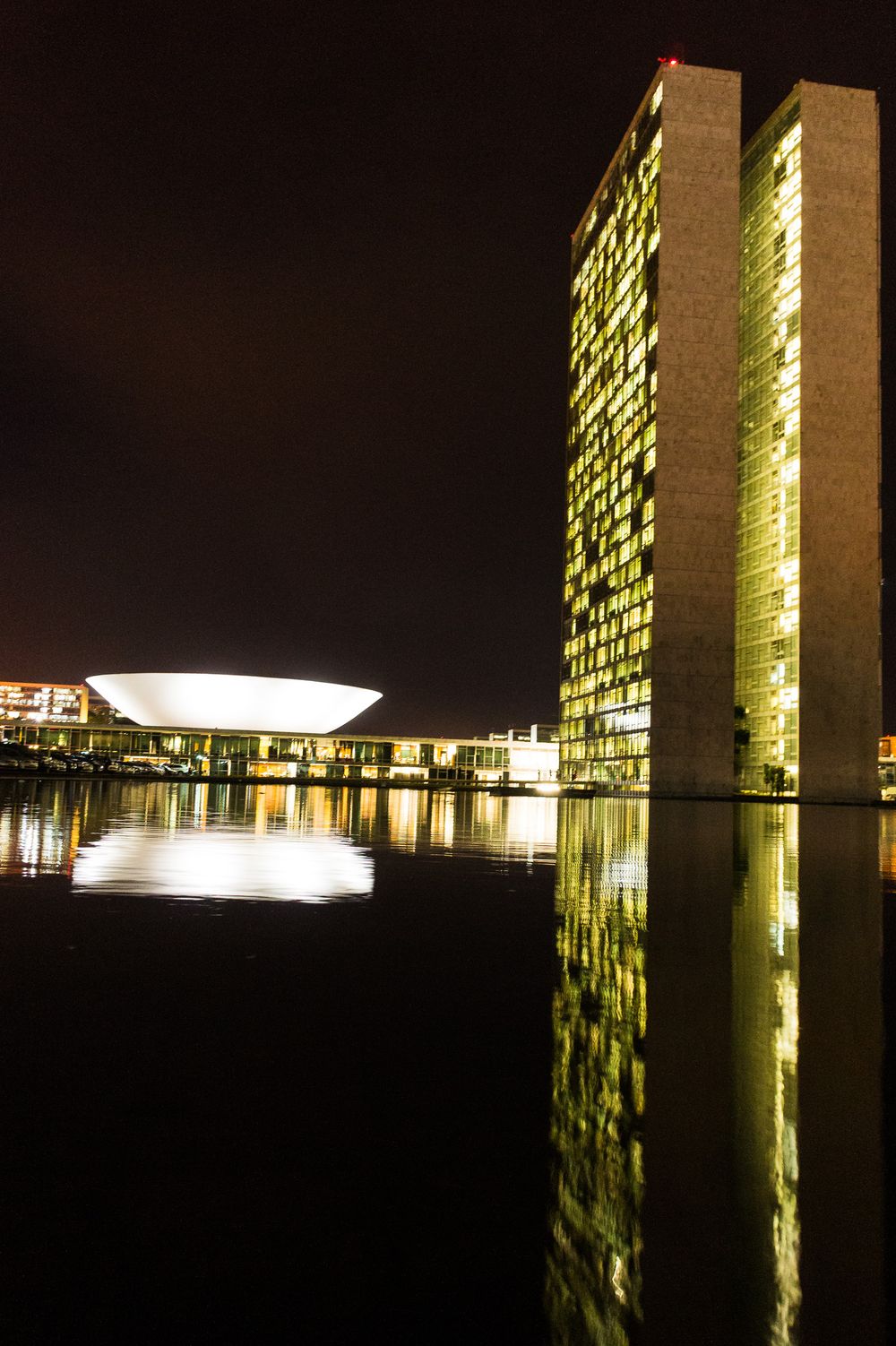 Night view of illuminated government buildings and their reflections in the water at the National Congress in Brasilia.