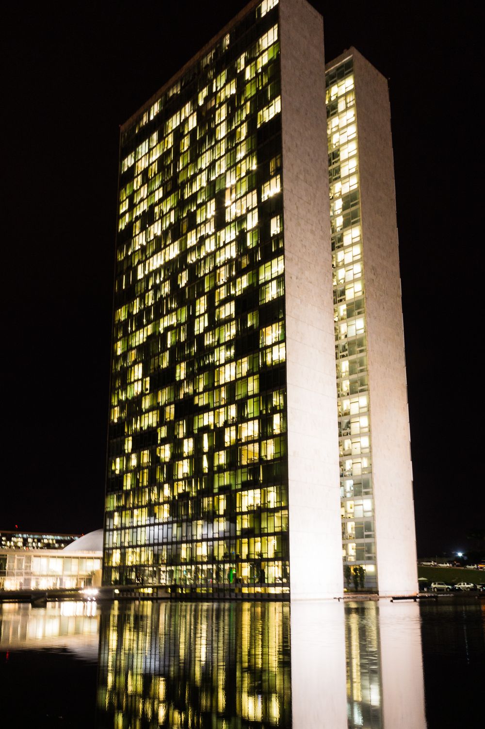 Modern high-rise building with illuminated windows reflecting in water at night creating dramatic architectural patterns.