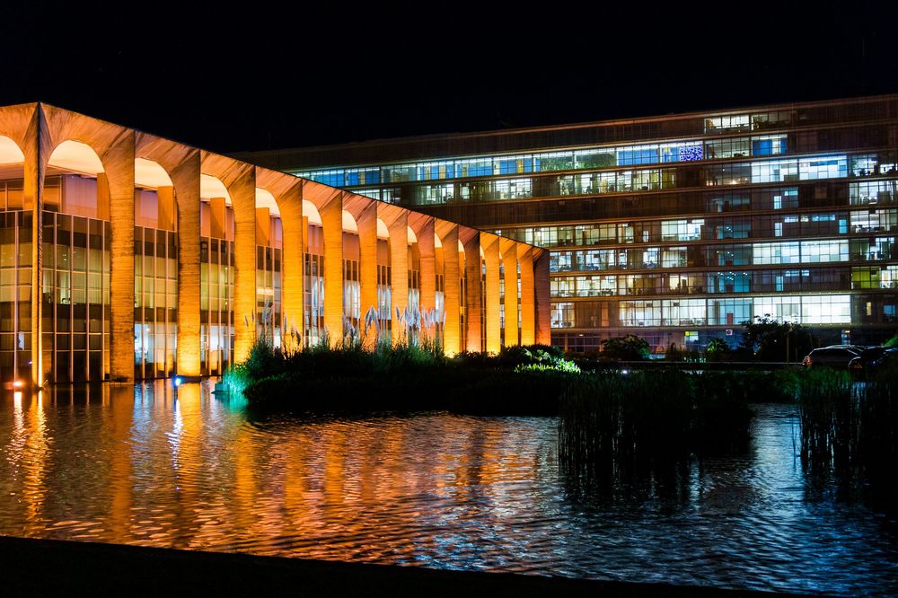 Illuminated waterfront buildings reflect on calm water at night creating a stunning mirror effect in city harbor.