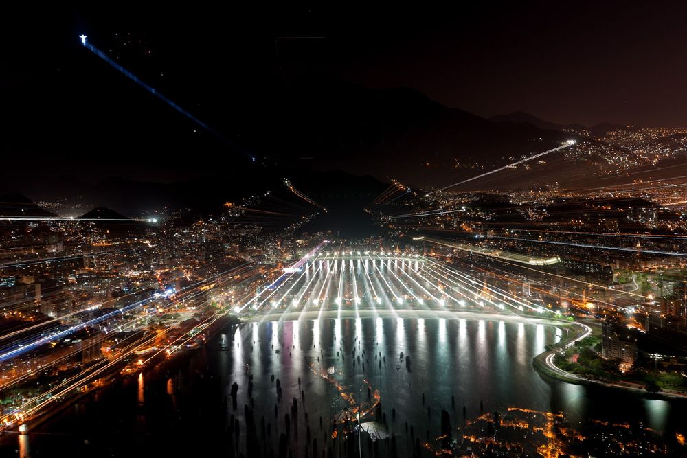 Illuminated hydroelectric dam at night with multiple waterfalls cascading down creating a dramatic light display.