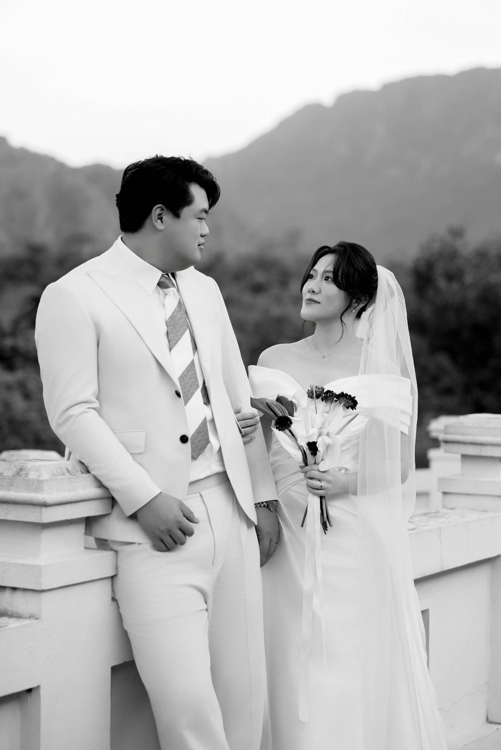 Black and white photo of wedding couple in white attire sharing a moment with mountain backdrop.