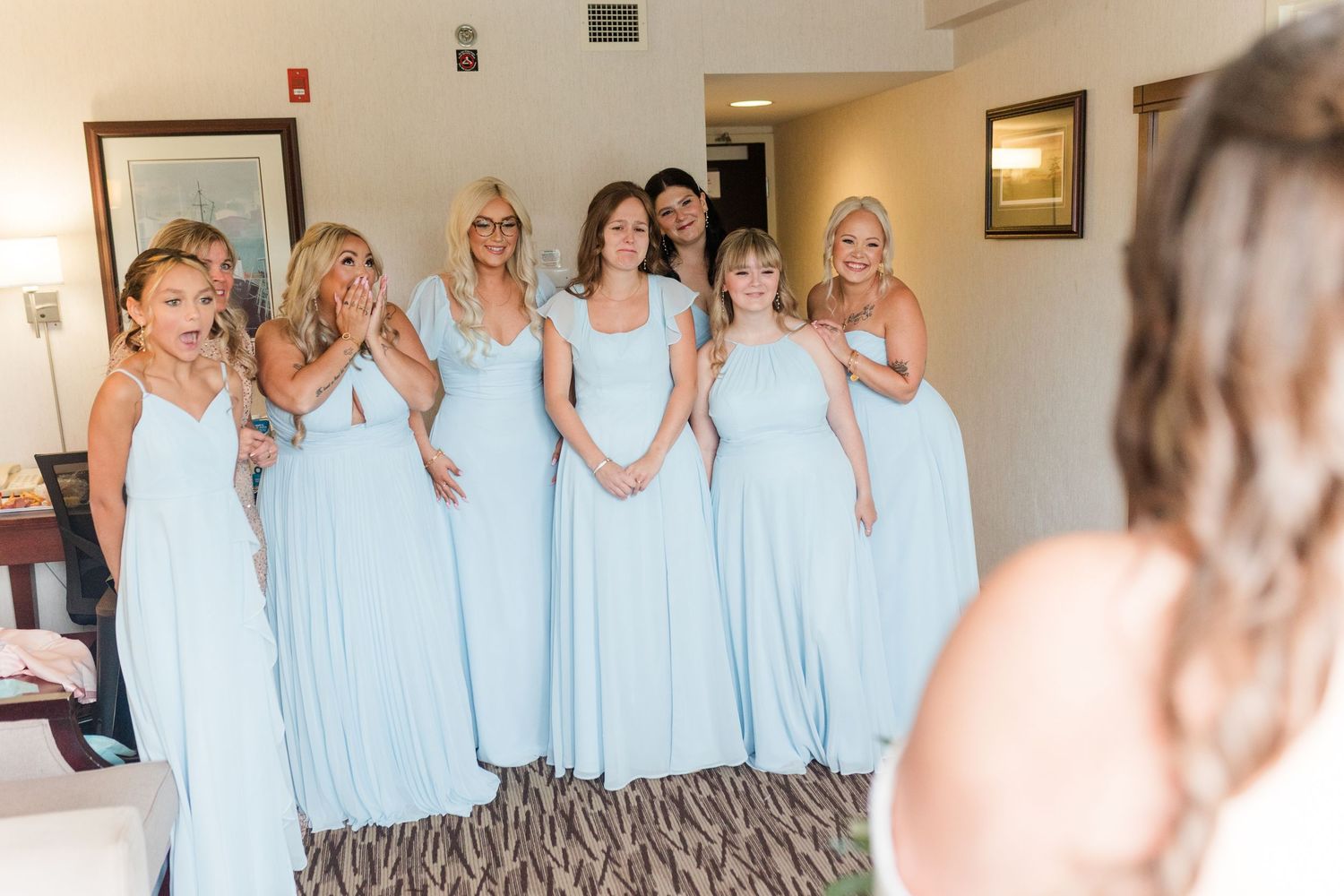 A row of bridesmaids wearing light blue dresses stand together at a wedding venue in matching outfits.