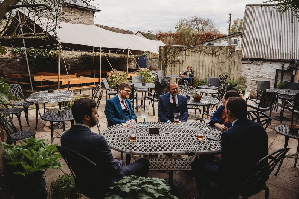 Group gathered around metal patio table at outdoor venue with string lights.