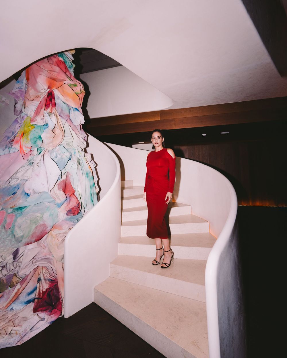 A series of four photos showing someone in a red dress descending white stairs with colorful fabric installations.