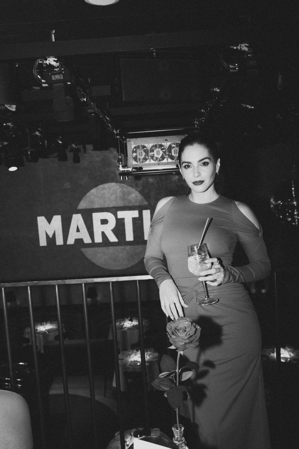 Black and white photo of a glamorous vintage-style scene at a bar with a Martini sign in the background.