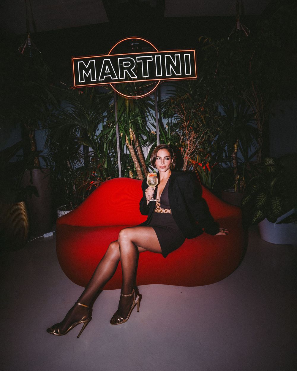 A dimly lit lounge setting with a red velvet couch and illuminated Martini sign creating a moody atmosphere.