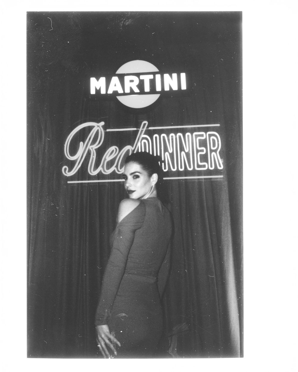 Vintage black and white performance photo with neon signs for Martini and other text visible in the background.