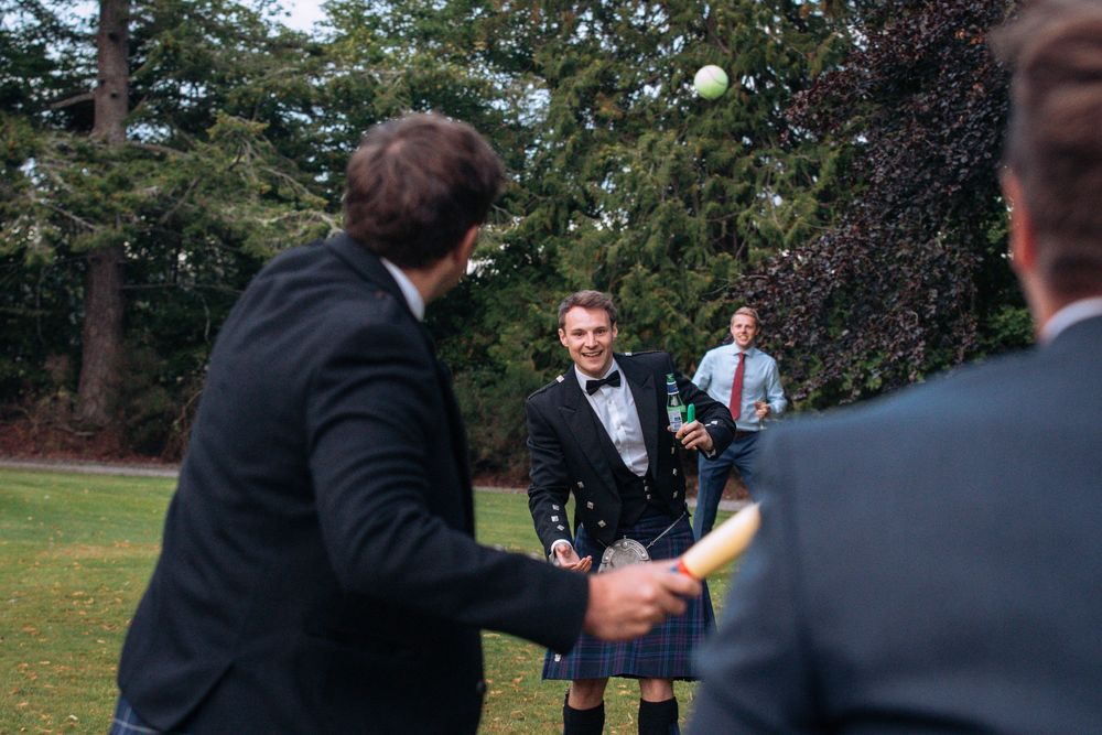 Wedding ceremony attendees gather outdoors under tall trees on a sunny afternoon during an intimate celebration.