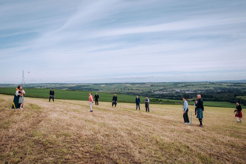 Hikers traverse rolling green hills under cloudy skies with expansive countryside views stretching to the horizon.