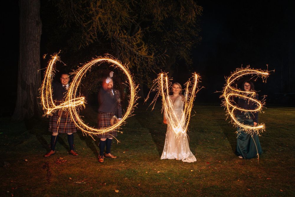 Long exposure photos show people creating light trails and patterns with sparklers in a dark outdoor setting at night.