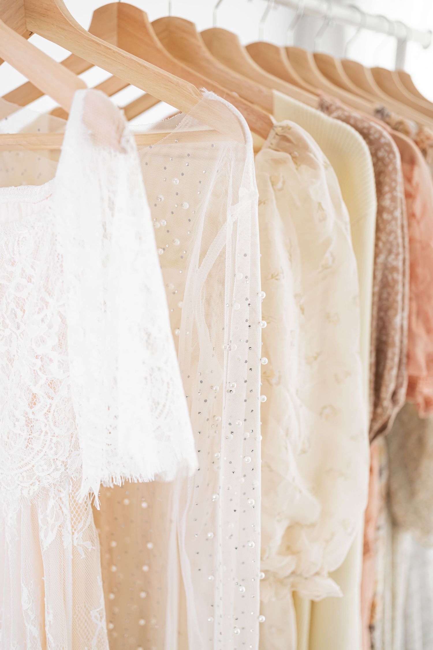 Delicate vintage-style dresses in soft pastel colors hanging on wooden hangers, featuring lace and polka dot details.