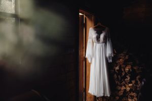 A flowing white wedding dress hangs illuminated in dramatic lighting near a wooden doorway.